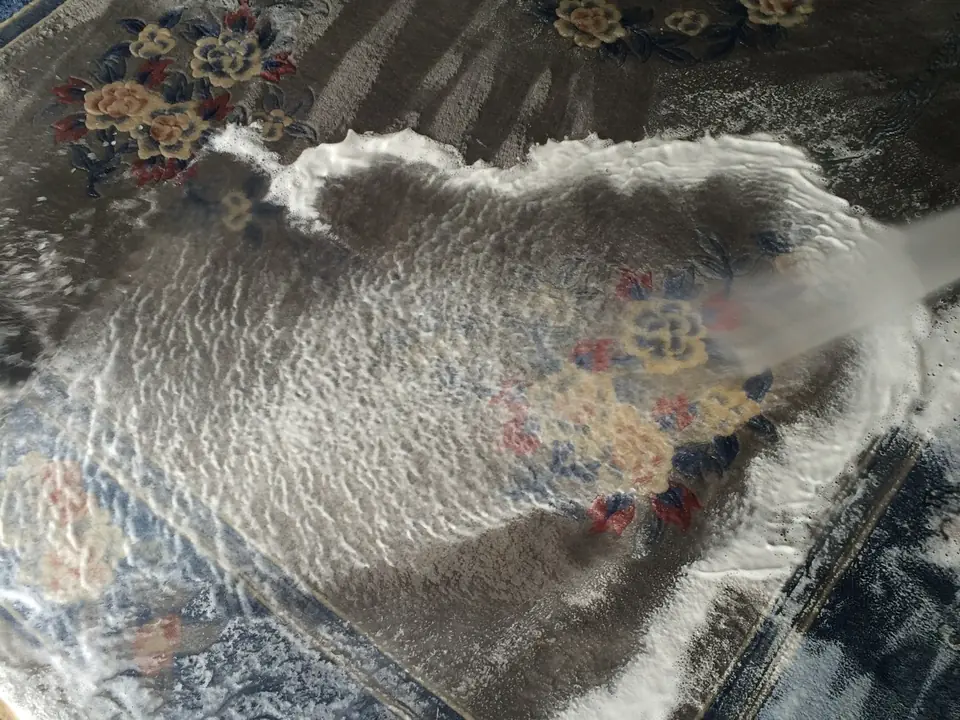 Ein Wasserstrahl spült den Schaum aus einem blauen Teppich mit Blumenmuster