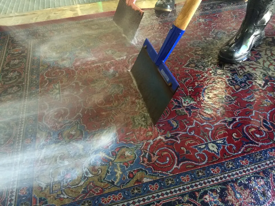 Mit einem Schieber wird das Wasser aus einem roten Perserteppich gedrückt