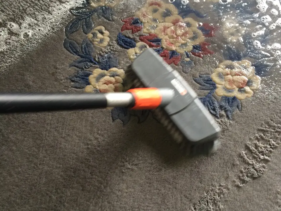 Ein heller Teppich mit Blumenmuster wird in der Wäscherei mit einer Bürste gewaschen