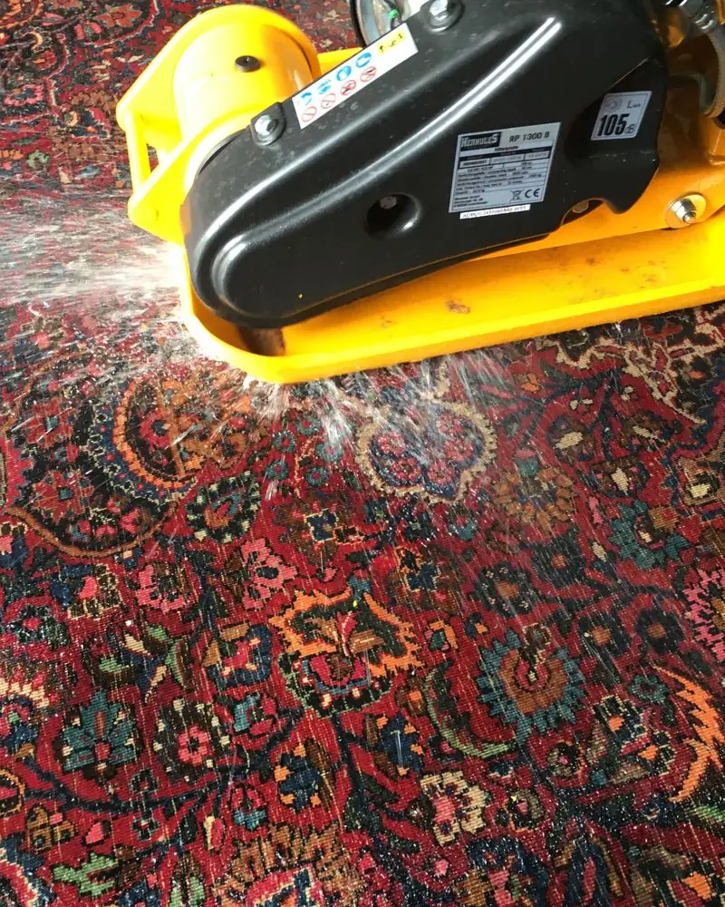Ein Klopfgerät treibt Staub und Sand aus einem roten Orientteppich