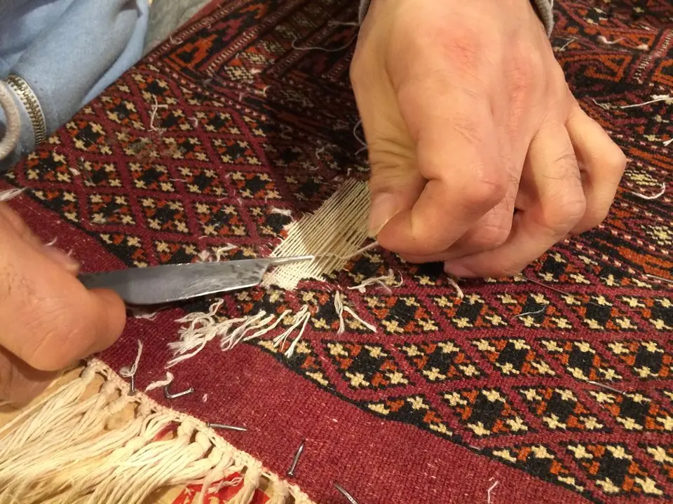Ein Restaurator arbeitet mit Messer und Garn am Rand eines roten Teppichs