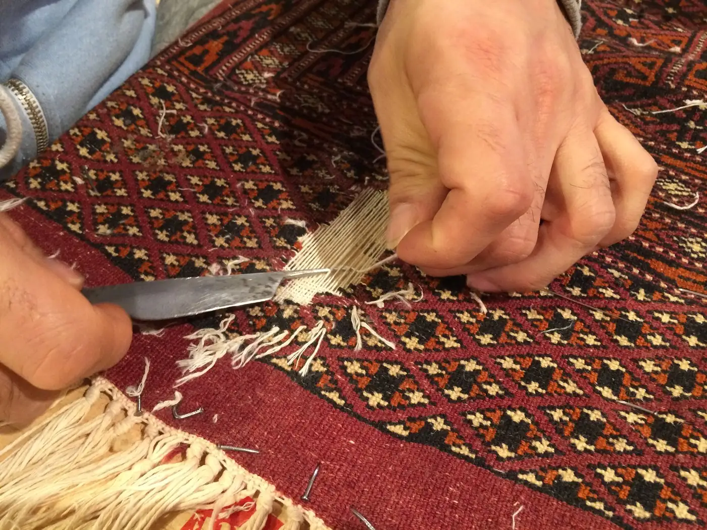 Ein Restaurator arbeitet mit Messer und Garn am Rand eines roten Orientteppichs