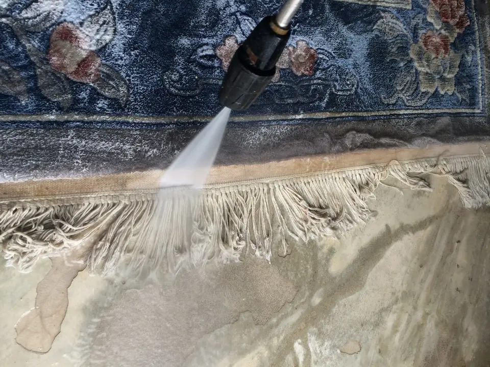 Die Fransen eines hellen Teppichs werden mit dem Wasserstrahl gewaschen