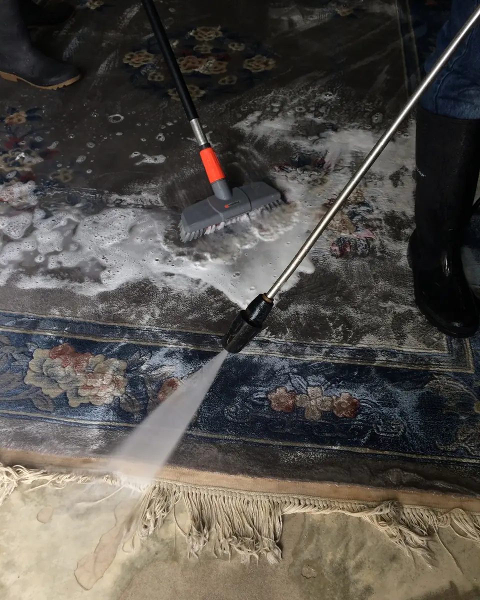 Ein blauer Teppich wird in der Wäscherei mit Bürste und Wasserstrahl gewaschen
